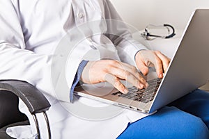 Mature doctor working on laptop and medication`s cases to make prescriptions in his clinic office. Man preparing online internet