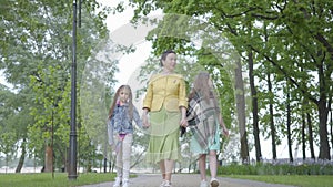 Mature elegant woman walking in the park with her two granddaughters. Happy family holding hands. Grandmother spending