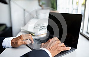 Mature european businessman in suit working on laptop with empty screen in modern office interior, cropped