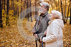 Mature european couple with nordic sticks walking in autumn park, enjoying the weather