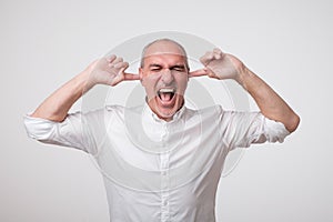 Mature european man closing his ears because of loud sound and noise. I do not want listen to you.