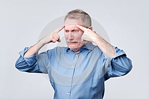 Mature european man holds fingers on temples, trying to remember something.