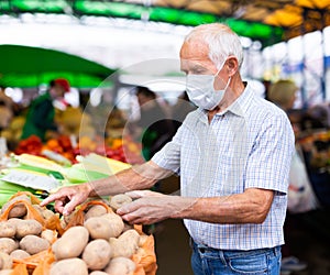 Mature european man wearing medical mask protecting against the virus buying potatoes in market