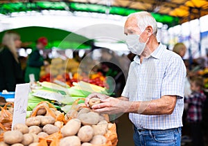 Mature european man wearing medical mask protecting against the virus buying potatoes in market
