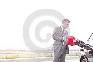 Mature executive fueling car with canister against sky