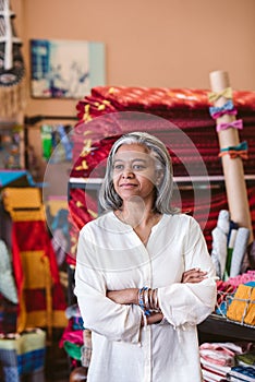 Mature fabric shop owner standing among her colorful textiles