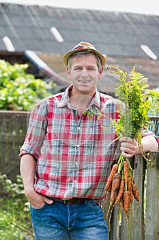 Mature farmer wearing hat while carrying carrots at barn