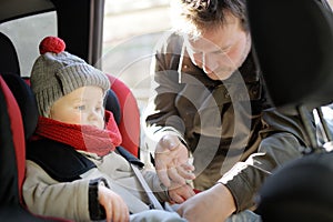 Mature father fastening his little son to the car seat. Dad takes care of the safety of baby boy during transportation. Child
