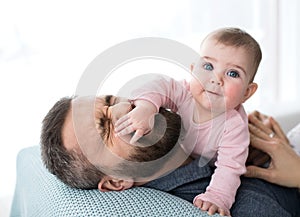 Mature father playing with baby daughter sitting indoors, having fun.