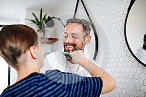 Mature father with small son in the bathroom in the morning, combing.