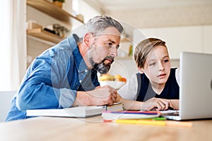 Mature father with small son sitting at table indoors, using laptop.