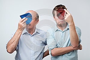 mature father and son hiding their face with birthday cap after great party having hangover