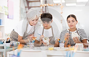 Mature female ceramicist teaching young couple to paint pottery in studio photo