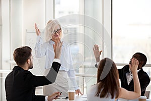 Mature female coach and employees rise hands involved in teambui