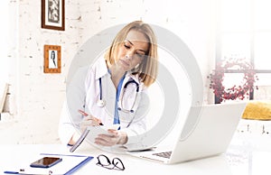 Mature female doctor doing making notes while working in doctor`s office photo