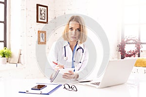 Mature female doctor doing making notes while working in doctor`s office photo