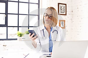 Mature female doctor text messaging and working on laptop