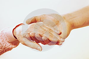 Mature female in elderly care facility gets help from hospital personnel nurse. Close up of aged wrinkled hands of senior woman. G