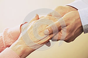 Mature female in elderly care facility gets help from hospital personnel nurse. Close up of aged wrinkled hands of senior woman. G