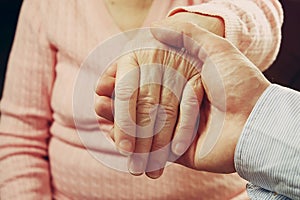 Mature female in elderly care facility gets help from hospital personnel nurse. Close up of aged wrinkled hands of senior woman. G