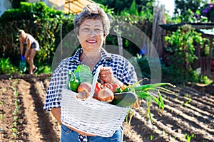 Mature female gardener posing with harvested vegetables