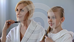 Mature female and granddaughter combing hair and smiling in front of mirror