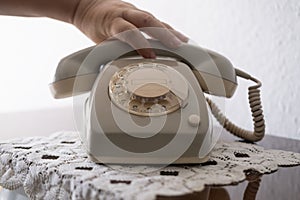 mature female hand removing Handset, rotating Dialer on Old white Rotary Telephone with Disc Dial with finger, putting retro phone