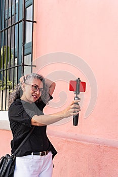 Mature female influencer smiling while broadcasting with her cell phone outdoors on the street