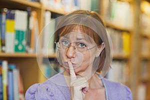 Mature female librarian giving a sign to be quiet standing in library