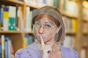 Mature female librarian giving a sign to be quiet standing in library photo