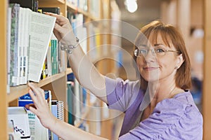 Mature female librarian taking a book off a shelf photo