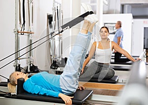 Mature female lying down on bed of Pilates reformer bed machine with legs up, working out and recovering in gym