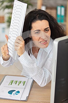 mature female office worker threatens to hit computer with keyboard