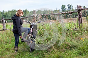 Mature female rider fasten her boots for riding dirt motorcycle in countryside, copy space