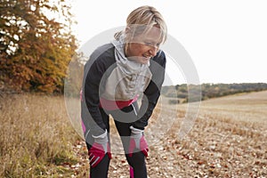Mature Female Runner Pausing For Breath During Exercise In Woods