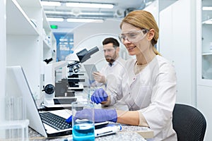 Mature female scientist in white coat at work, laboratory assistant using microscope and laptop at work, scientist