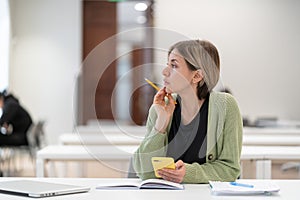 Mature female student taking second degree looking through window and dreaming, studying in library