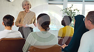 Mature female teacher giving lecture to group of multinational students in classroom