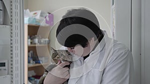 Mature female veterinarian in white gown holding on arms cute nervous cat, trying to calm animal, touching his nose with