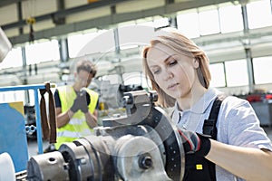 Mature female worker working on machinery with colleague in background at industry