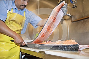 Mature fishmonger slicing salmon fish on table