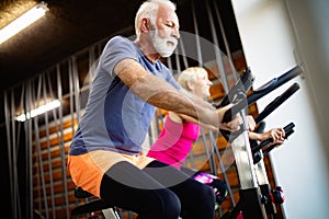 Mature fit people biking in the gym, exercising legs doing cardio workout cycling bikes