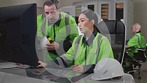 Mature foreman in uniform help young asian woman engineer working on computer