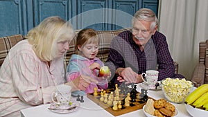 Mature grandmother grandfather with child girl grandchild playing chess game with on table in room