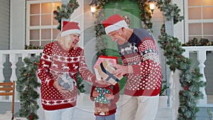 Mature grandparents family with granddaughter exhcanging gifts boxes presents for Christmas at home