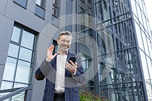 Mature gray-haired businessman talking video call, man using smartphone app to communicate with friends and colleagues