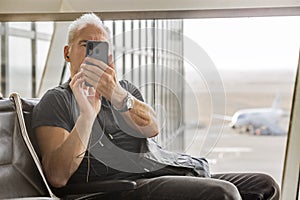 A mature gray-haired man takes pictures on his smartphone in the departure hall of the airport. Business trip.