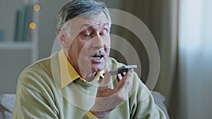 Mature grey-haired 60s man 70s senior old male at home hold smartphone speak loud to phone microphone speaker audio