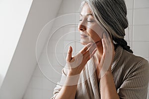 Mature grey woman getting facial massage in bathroom