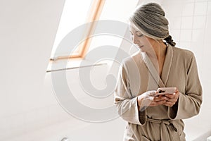 Mature grey woman using mobile phone in bathroom